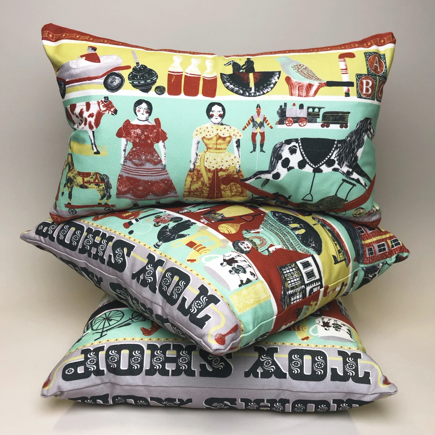 A trio of Abbey House Museum cushions displaying a design of victorian toys