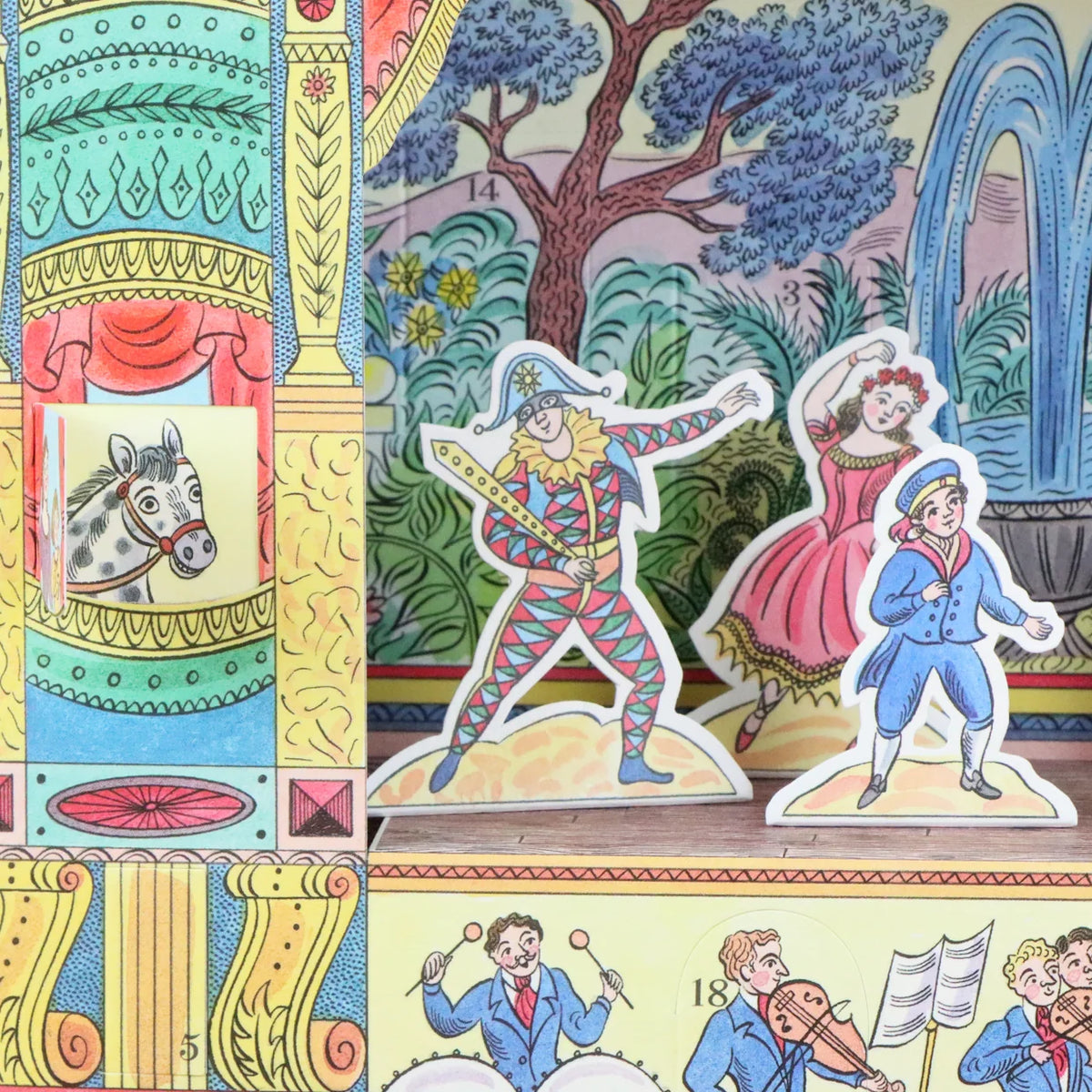 A close-up of a vintage inspired Pantomime advent calendar showing colorful printed scenery, decorative columns, and die-cut character pieces including a dancer, a woman in a pink dress, and musicians.