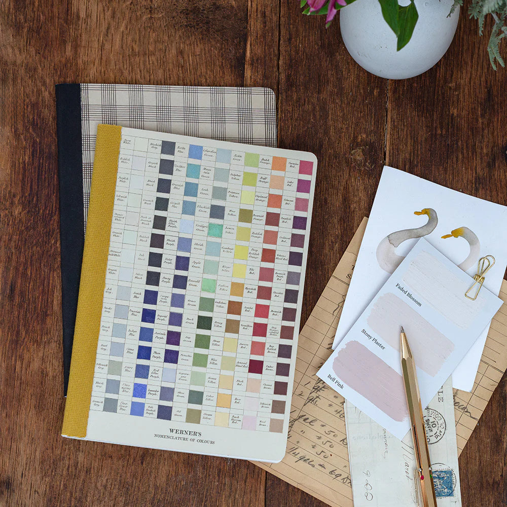 Color swatch book, stationery items, and a pen on a wooden surface.