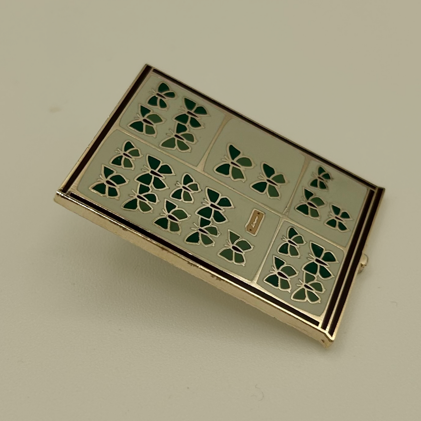 Decorative pin badge with green butterfly pattern on a beige background