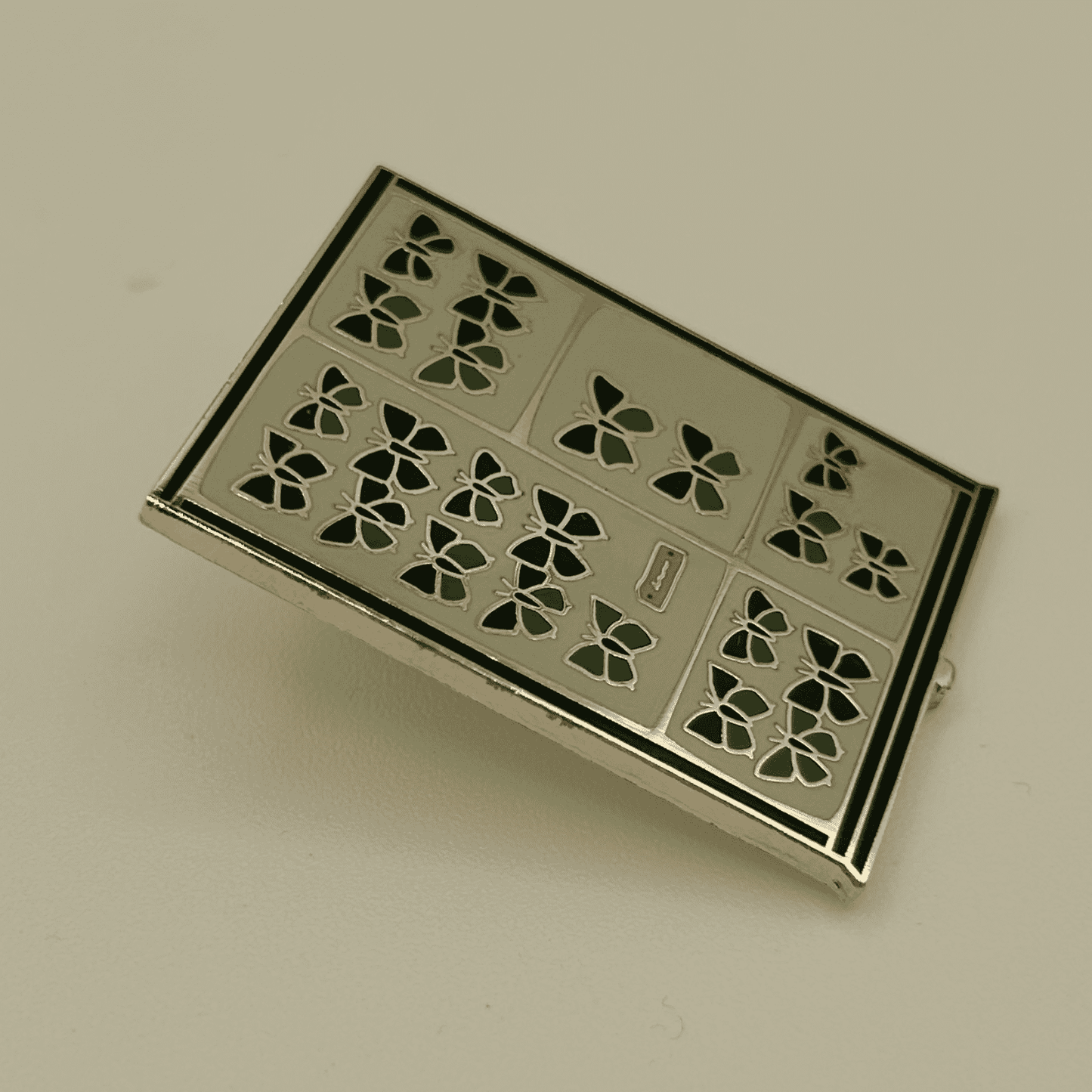 Decorative pin badge with green butterfly pattern on a beige background