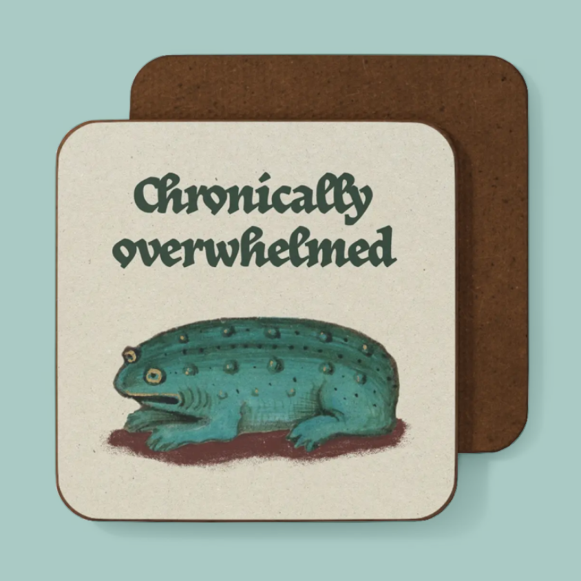 A square coaster with rounded corners featuring the text 'Chronically overwhelmed' above an illustration of a teal amphibian creature, shown in front of a second coaster on a light aqua background.
