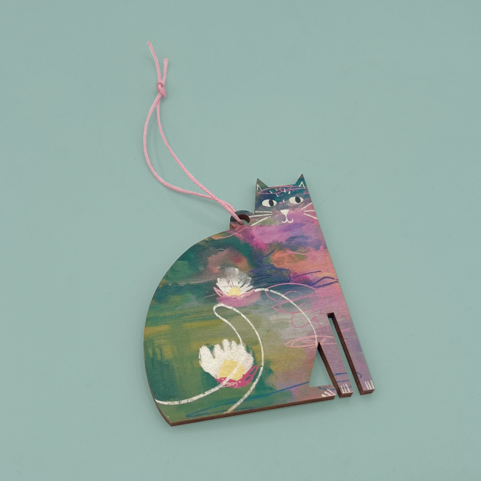 A wooden cat-shaped ornament with a colorful watercolor-style painting of a pond and lily pads, attached to a pink string, shown on a solid light blue background.