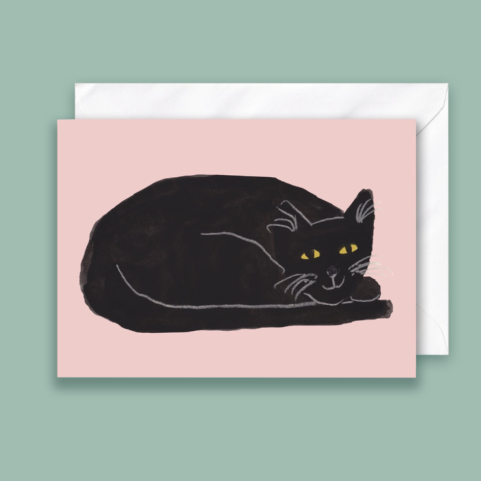 A rectangular card featuring a black cat curled up on a pale pink background, with a white envelope behind it on a muted green backdrop.