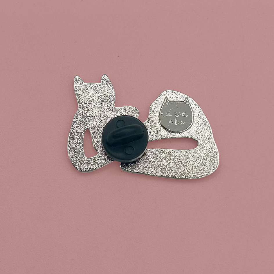 The back of a silver lapel pin with a black rubber backing, displayed on a solid dusty pink background.