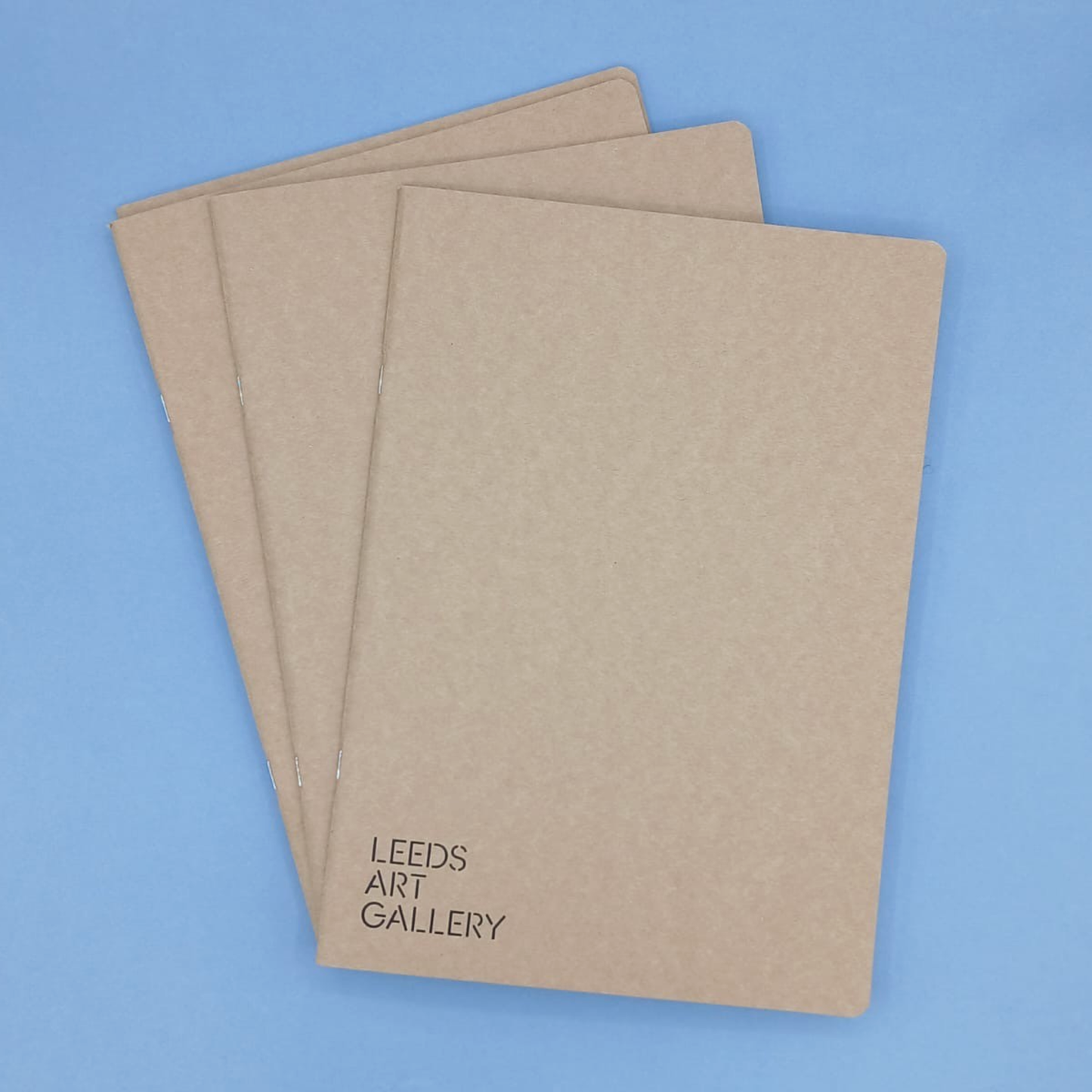 Three brown notebooks with 'Leeds Art Gallery' text on a blue background