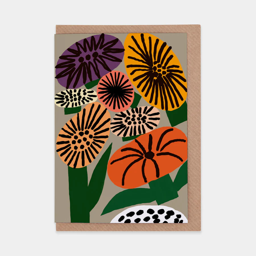A portrait orientation greetings card with a digital illustration of colourful flowers on a beige background. The card is on a brown envelope on a plain backdrop.