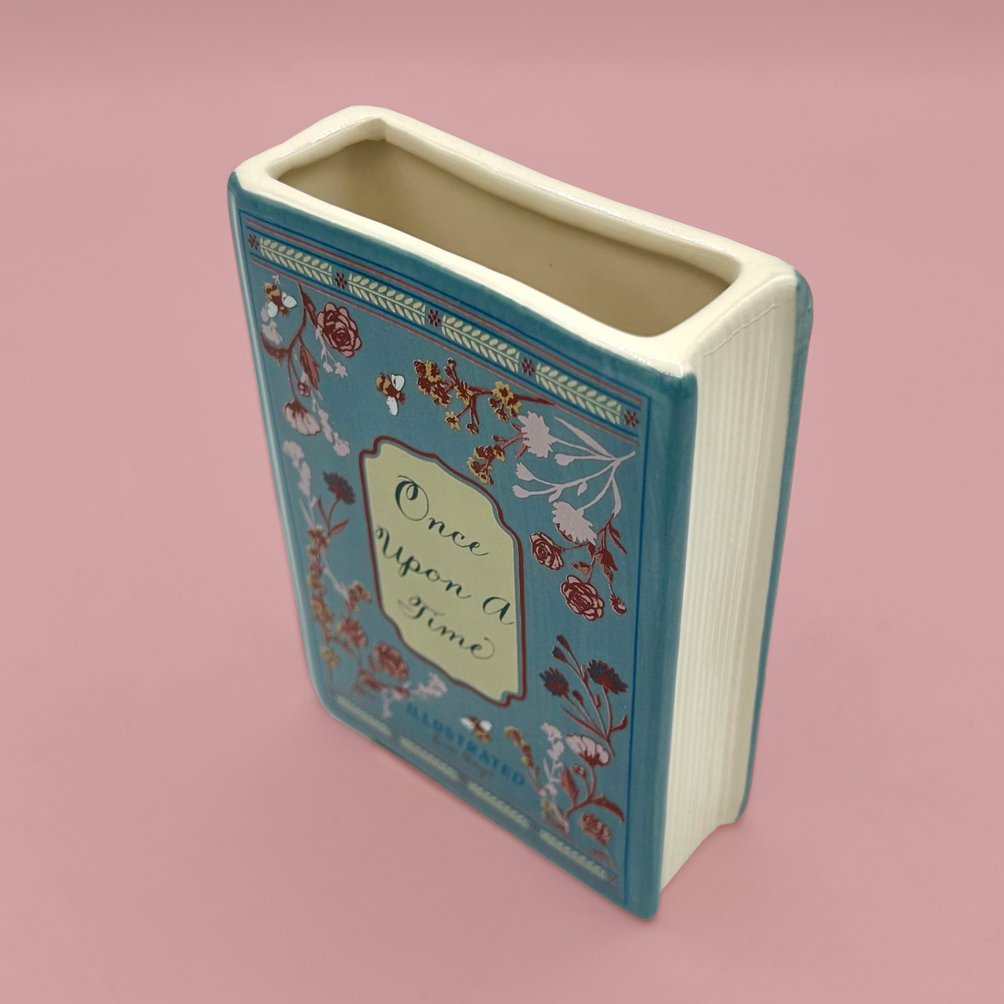 Decorative vase shaped like a book with floral designs and 'Once Upon A Time' text on a pink background