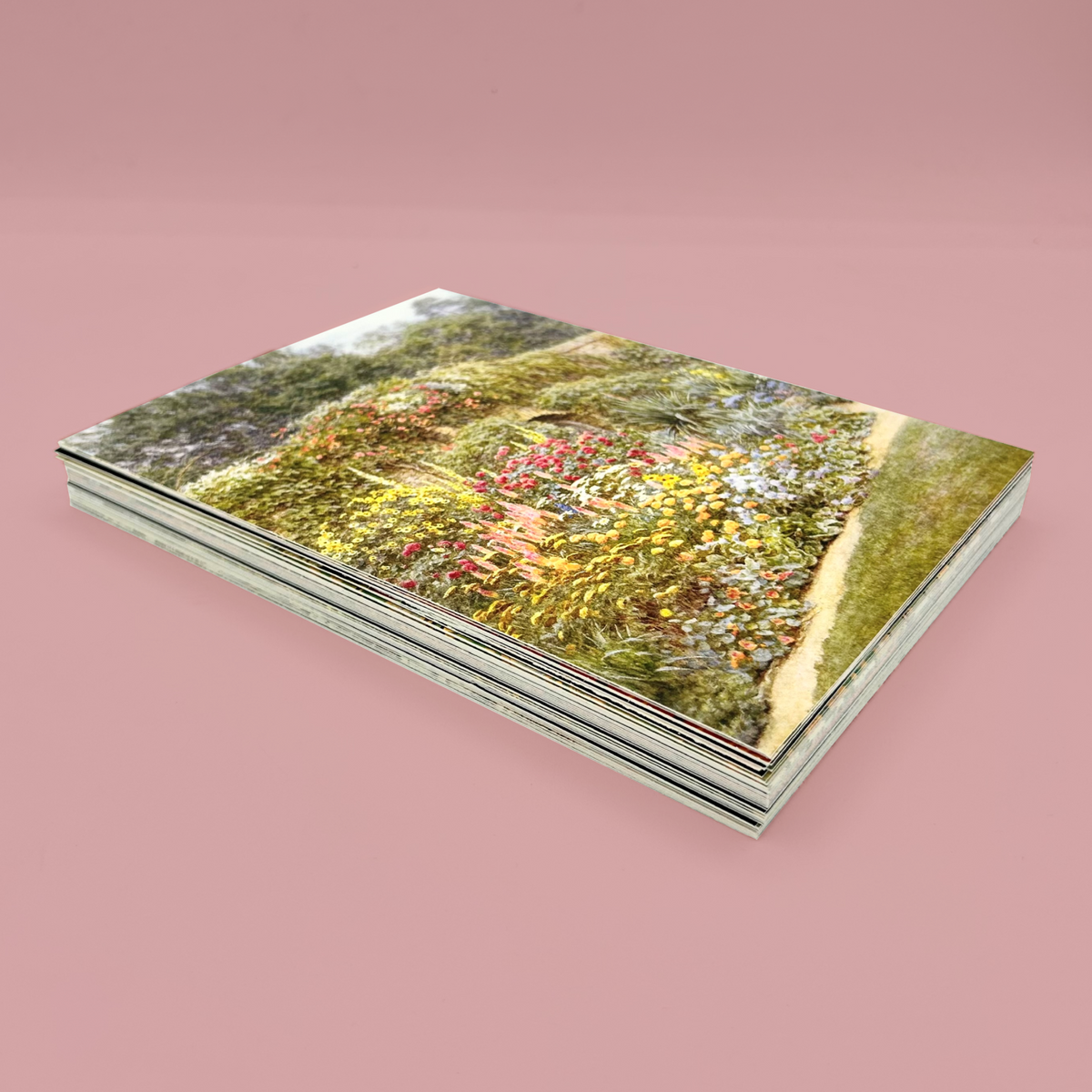 Stack of postcards, the top one features a garden scene. The stack is on a pink background