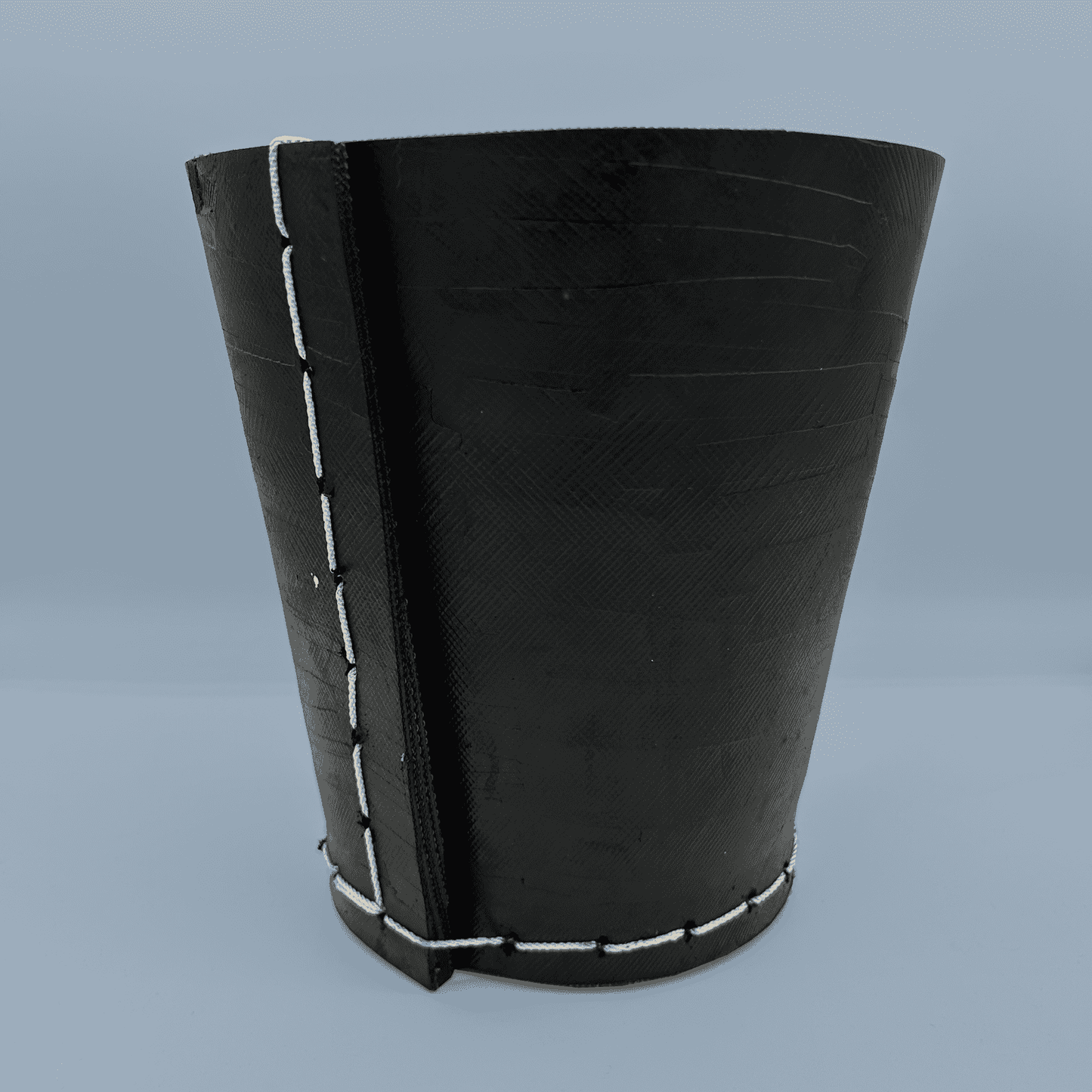 Black rubber plant pot with white stitching on a blue background