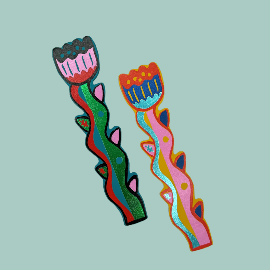 Two colourful and shiny flower-shaped leather bookmarks on a blue background.