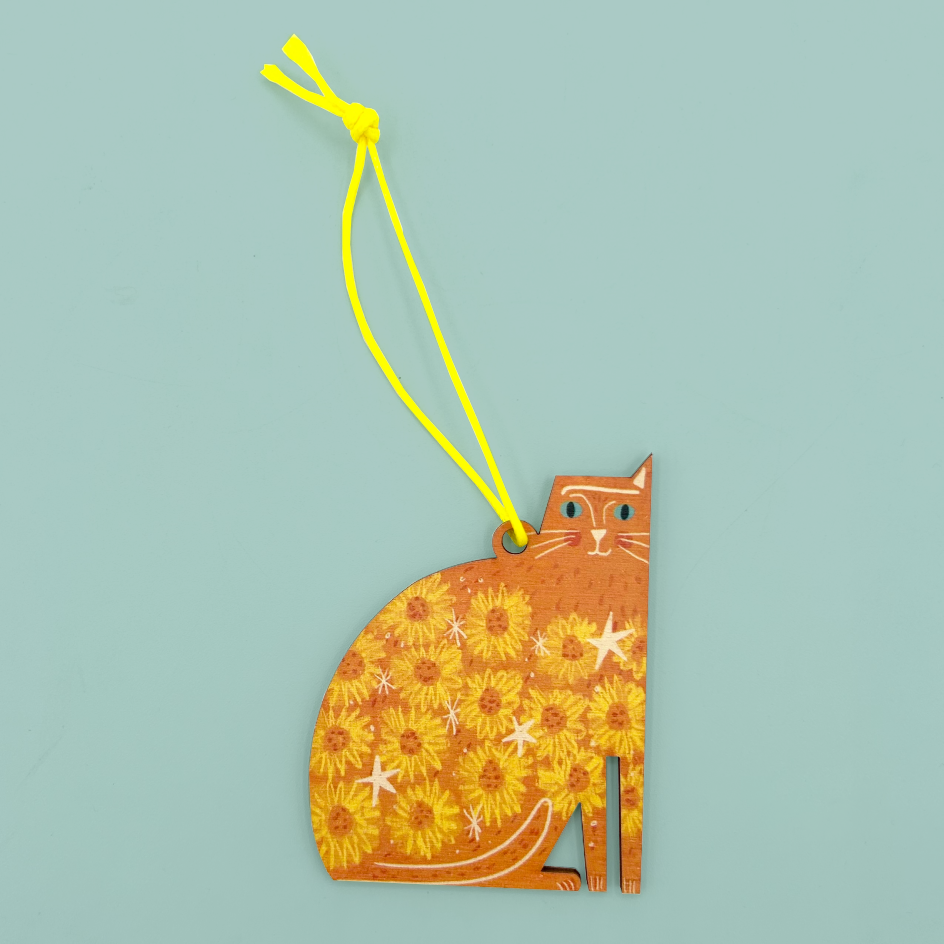 Orange cat shaped hanging ornament with flower and star embellishments and one ear. The decoration is hanging from a neon yellow string.