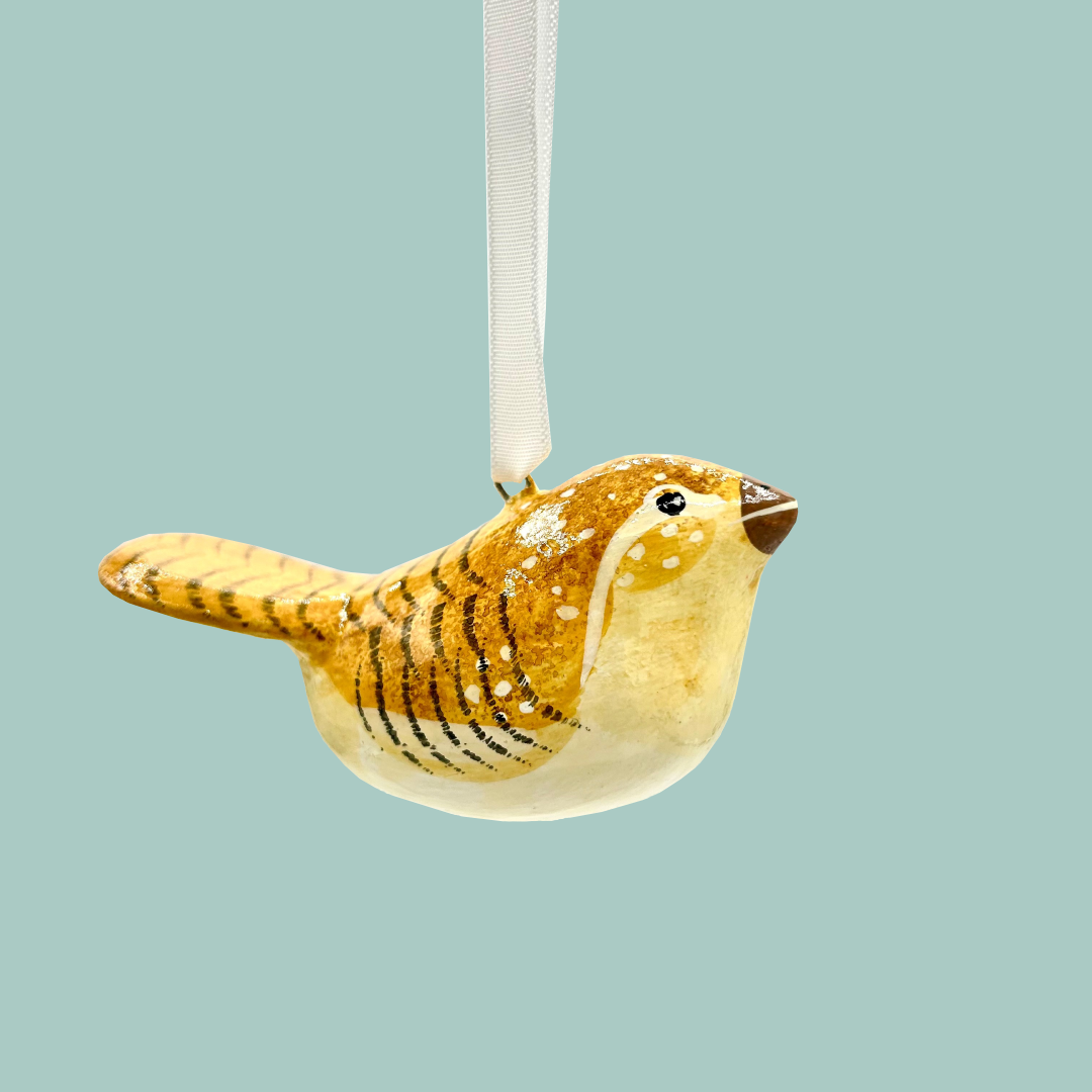 A pale yellow ochre painted bird hanging on a blue background.