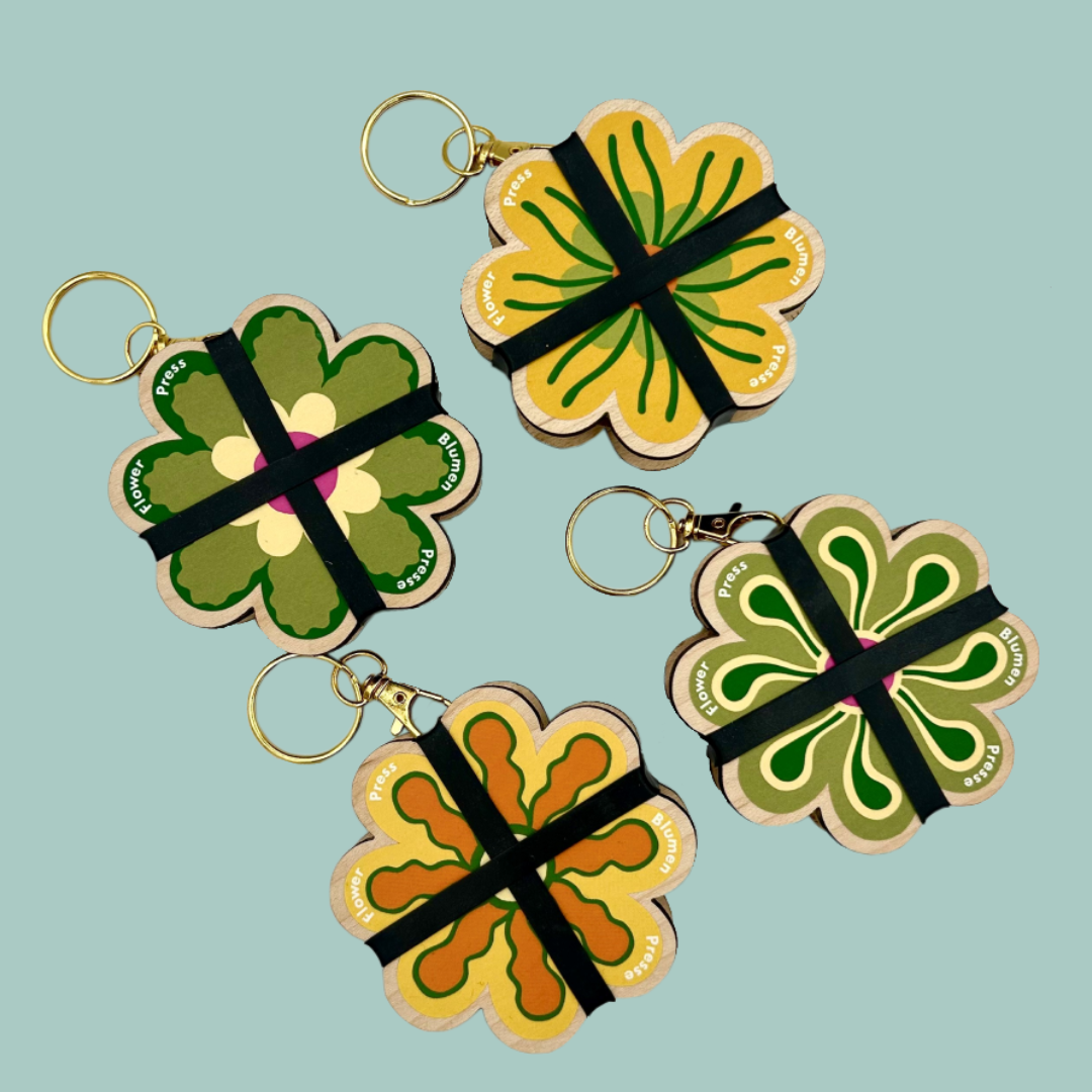 Four yellow and green flower shaped flower presses with gold keychains on a blue background.