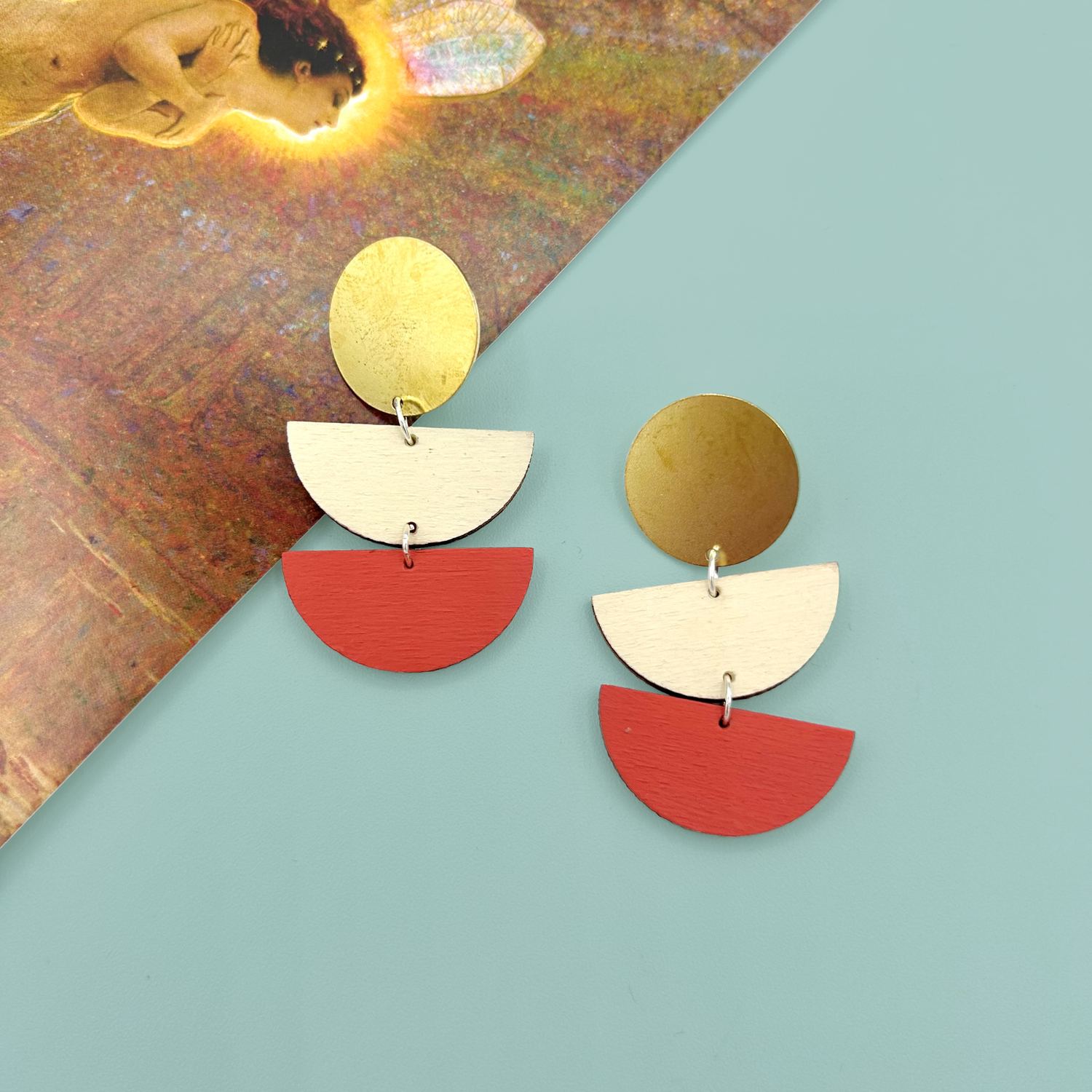 A brown background with a paid of green abstract earrings in the middle surrounded by other metal earrings and necklaces