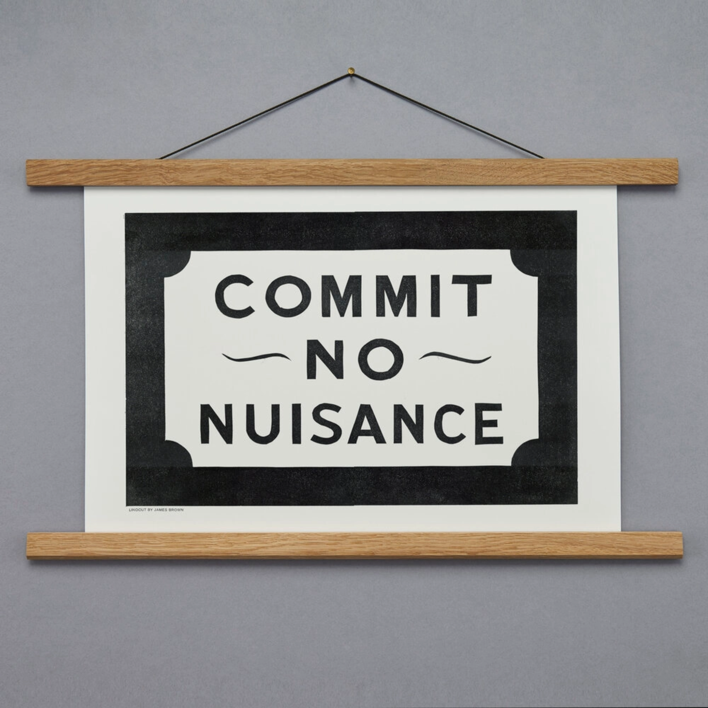 Hanging print with 'Commit No Nuisance' text on a gray background