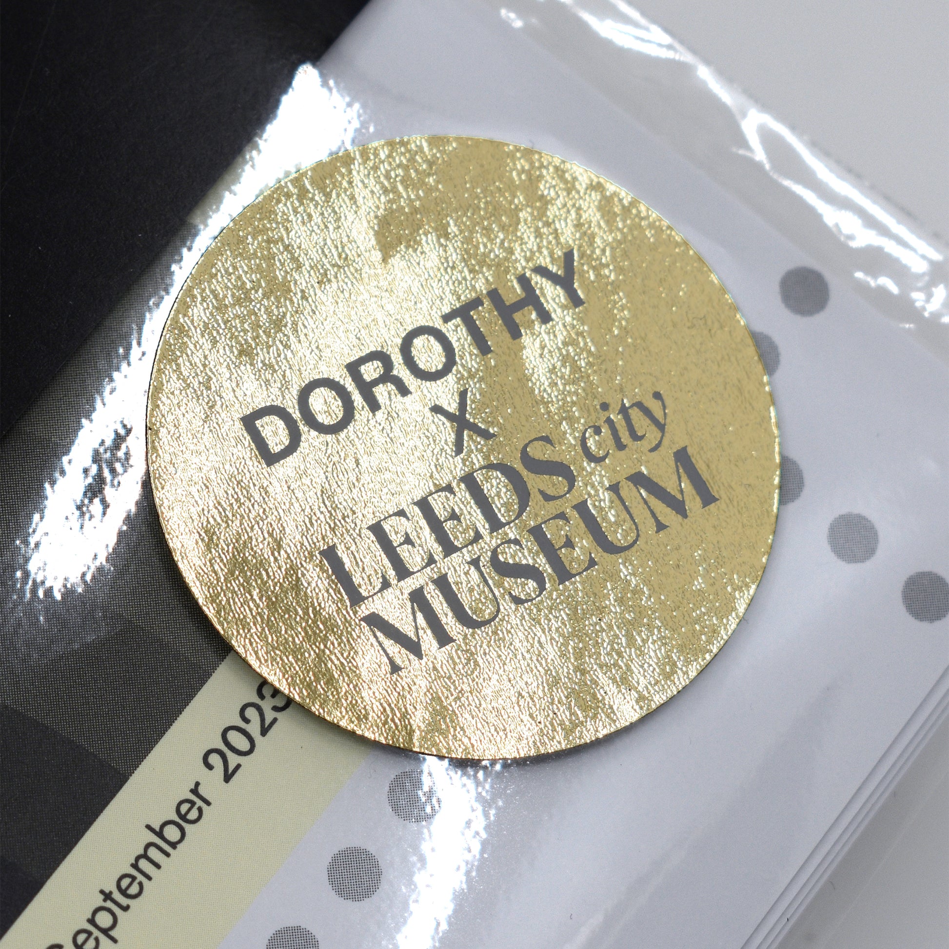 Gold circular label with 'DOROTHY x LEEDS city MUSEUM' text on a white background.