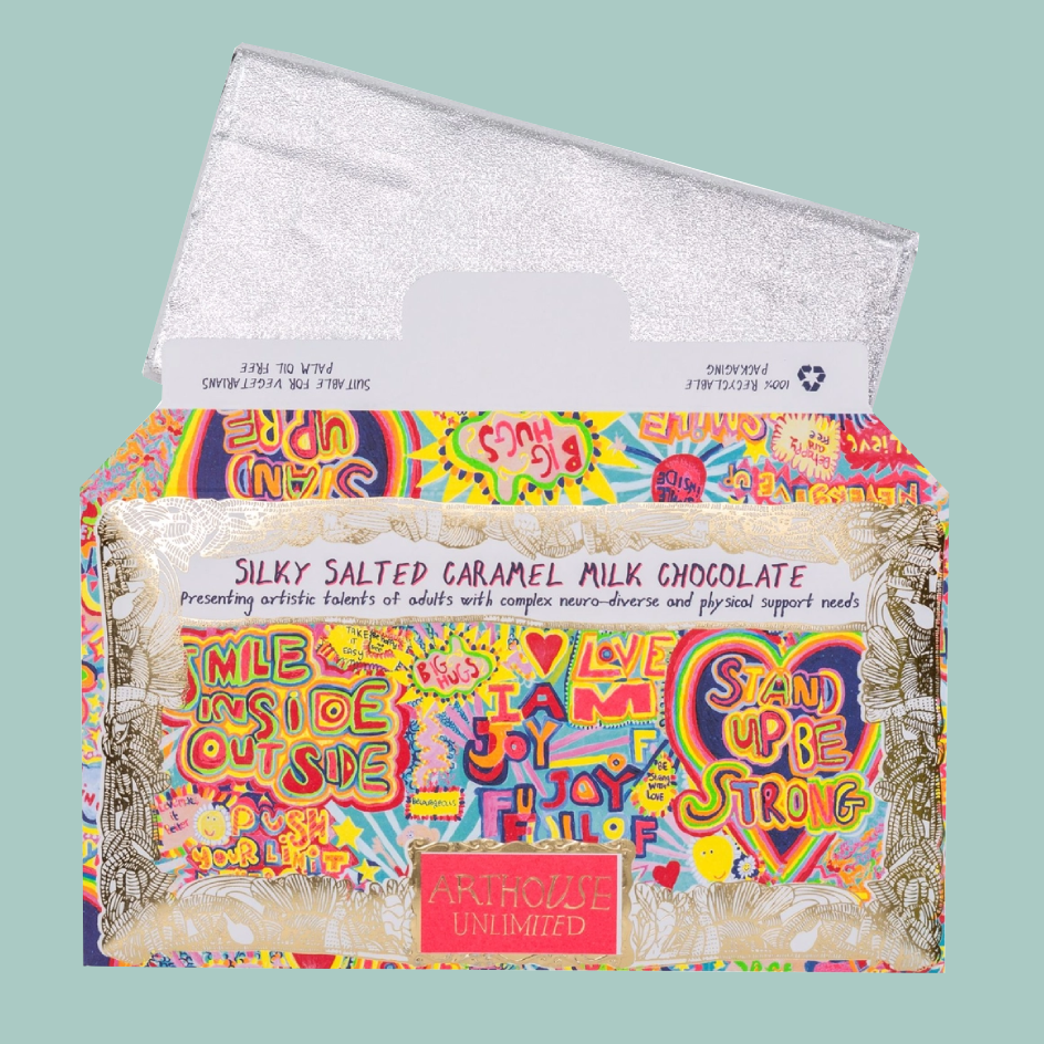 A boxed chocolate bar package with a bright multicolor graffiti-style label and a silver glittery wrapper, shown on a pale mint background. The front text reads 'Silky Salted Caramel Milk Chocolate' and the brand name 'Arthouse Unlimited' appears on a pink label near the bottom.