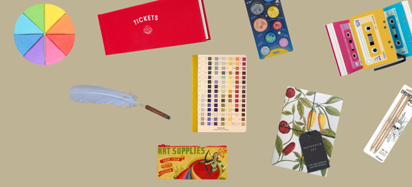 Collection of stationery items including a red notebook, colorful feathers, and various small boxes on a beige background.