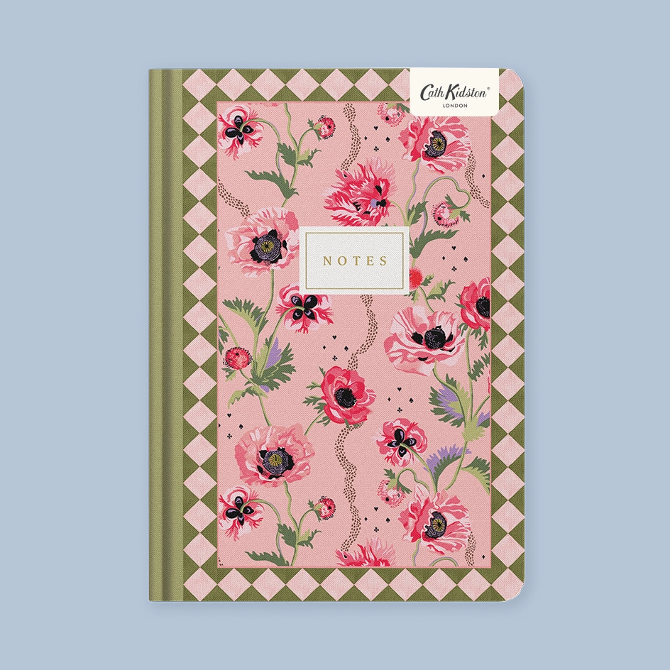 A pink floral patterned notebook with a green and pink diamond border, featuring a white 'Cath Kidston London' brand sticker and a central white 'NOTES' label, shown on a light blue background.