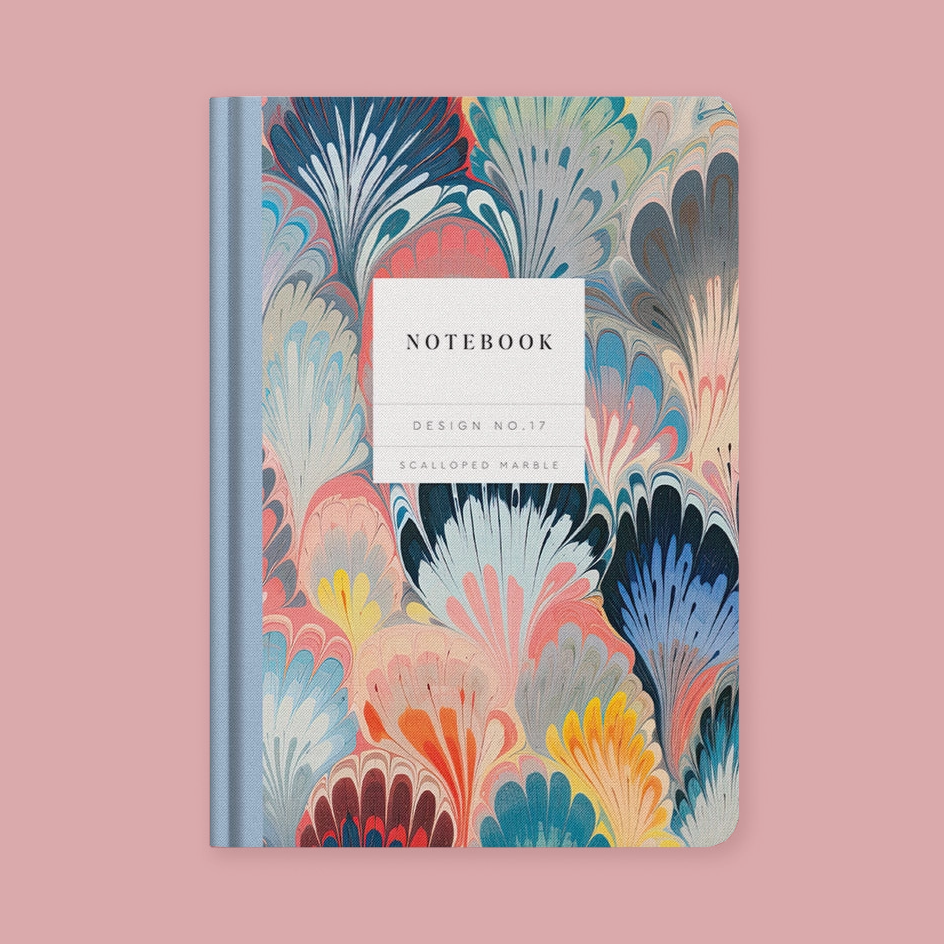 A notebook with a colorful marbled cover pattern in shades of blue, pink, yellow, and beige, featuring a white label in the center that reads 'NOTEBOOK' and 'DESIGN NO.17 SCALLOPED MARBLE'.