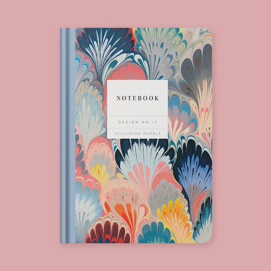 A notebook with a colorful marbled cover pattern in shades of blue, pink, yellow, and beige, featuring a white label in the center that reads 'NOTEBOOK' and 'DESIGN NO.17 SCALLOPED MARBLE'.