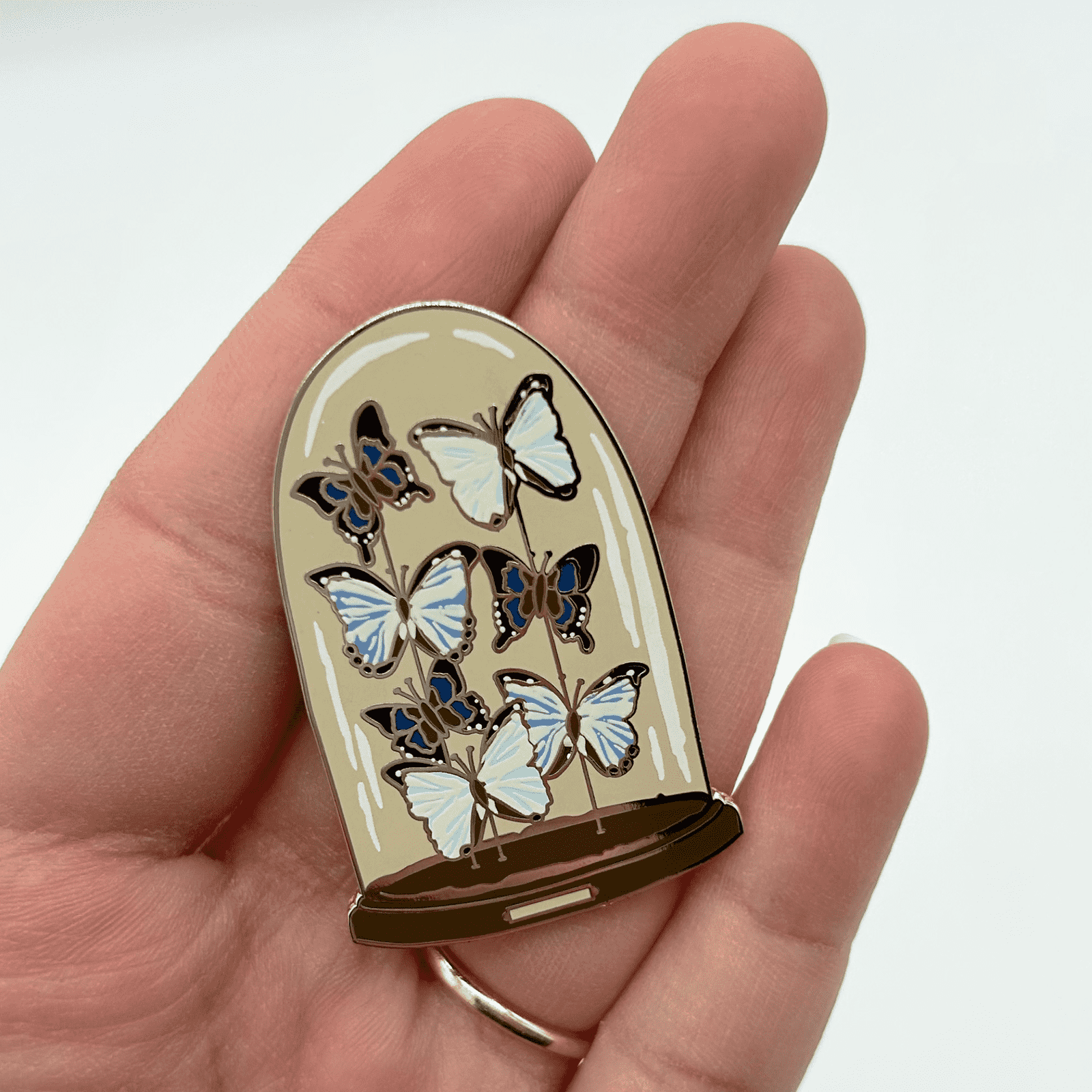 Butterfly-themed pin held in a hand against a white background