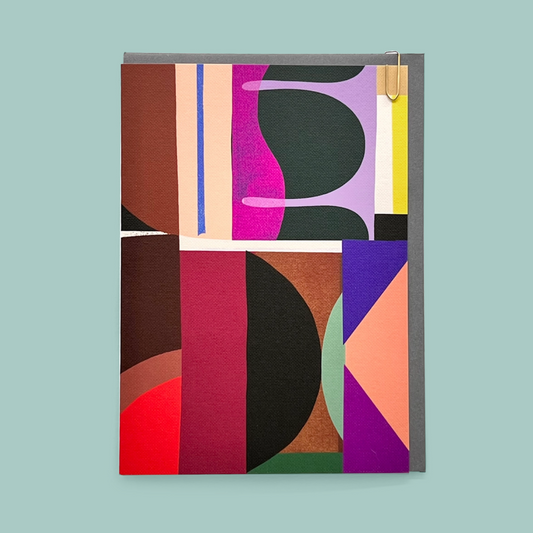 Colorful geometric patterned greetings card with grey envelope on a light blue background.