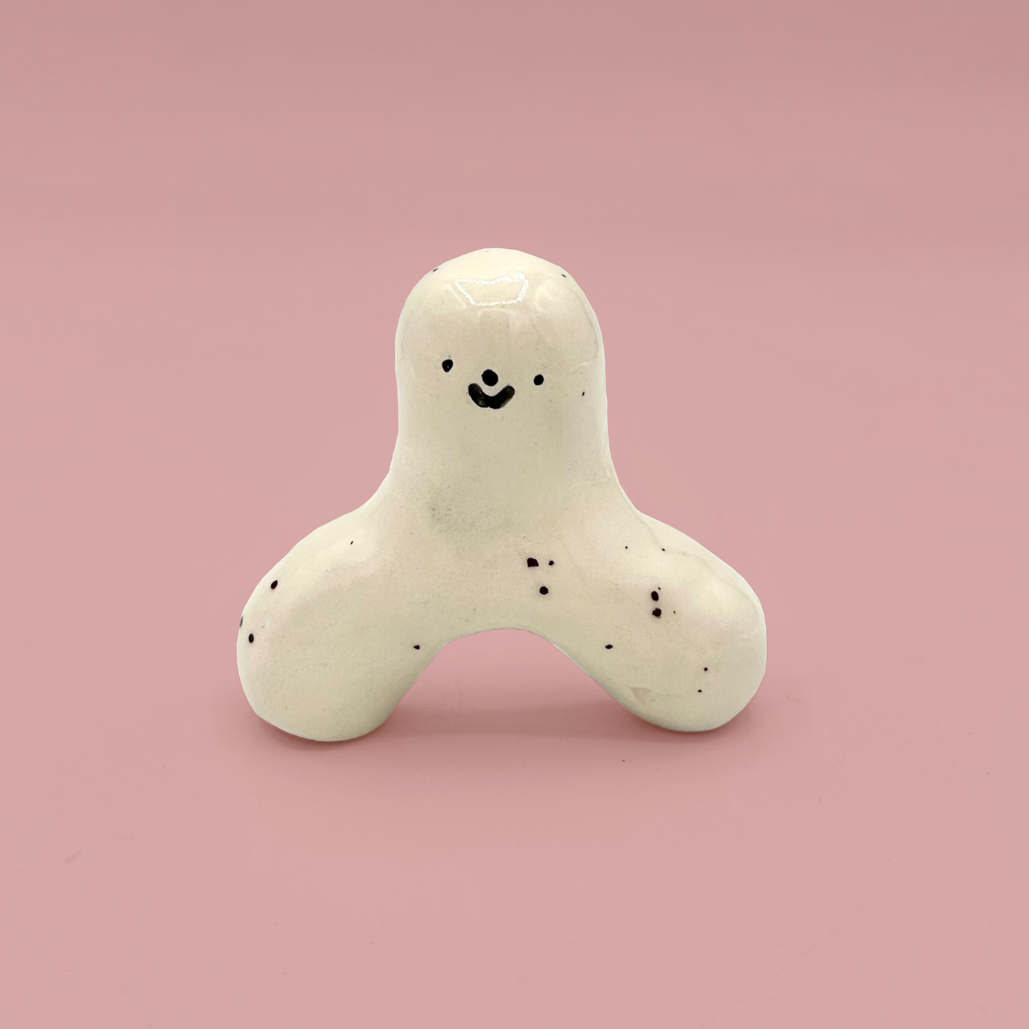 White ceramic figure with smiling face and black spots on a pink background
