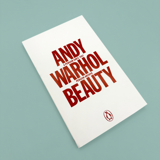 Book titled 'Andy Warhol Beauty' with red text on a white background. he book is on a blue background.