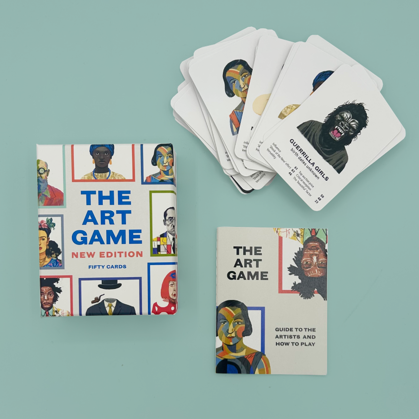 The Art Game New Edition card deck and guide set arranged on a light blue background, with the box on the left, a fan of illustrated cards on the upper right, and the instruction booklet on the lower right.
