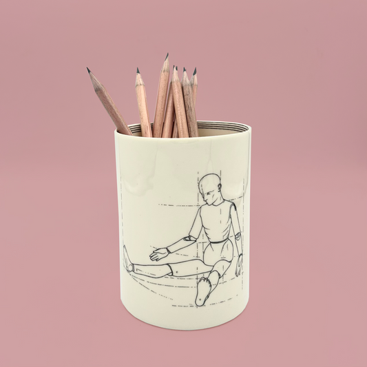 Pencil holder with a design of an artist's model sitting, filled with pencils, on a pink background.