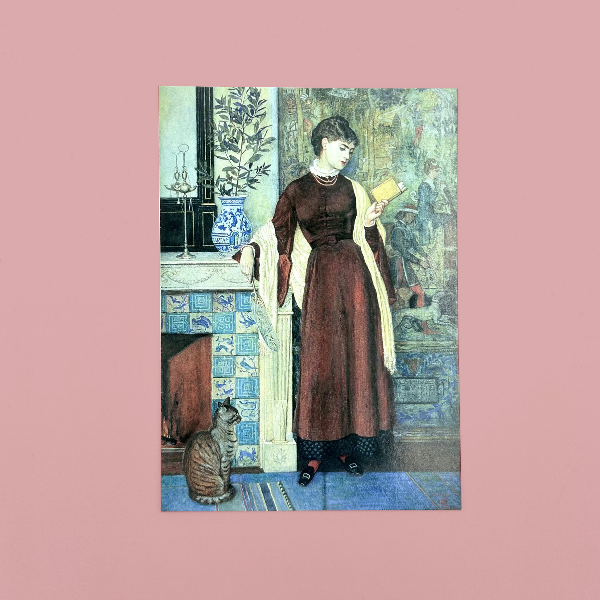Postcard of At Home: A Portrait by Walter Crane which features a woman in a room with a cat. The postcard is on a pink background
