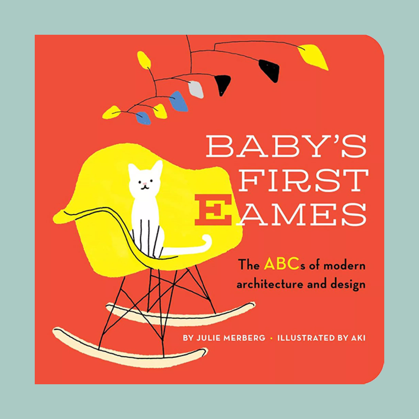 Book cover for 'Baby's First Ames: The ABCs of modern architecture and design' by Julie Merberg, illustrated by Aki. The cover features a bold coral-red background with a yellow rocking chair, a white cat, and modern abstract tree branches in yellow, blue, black, and white.