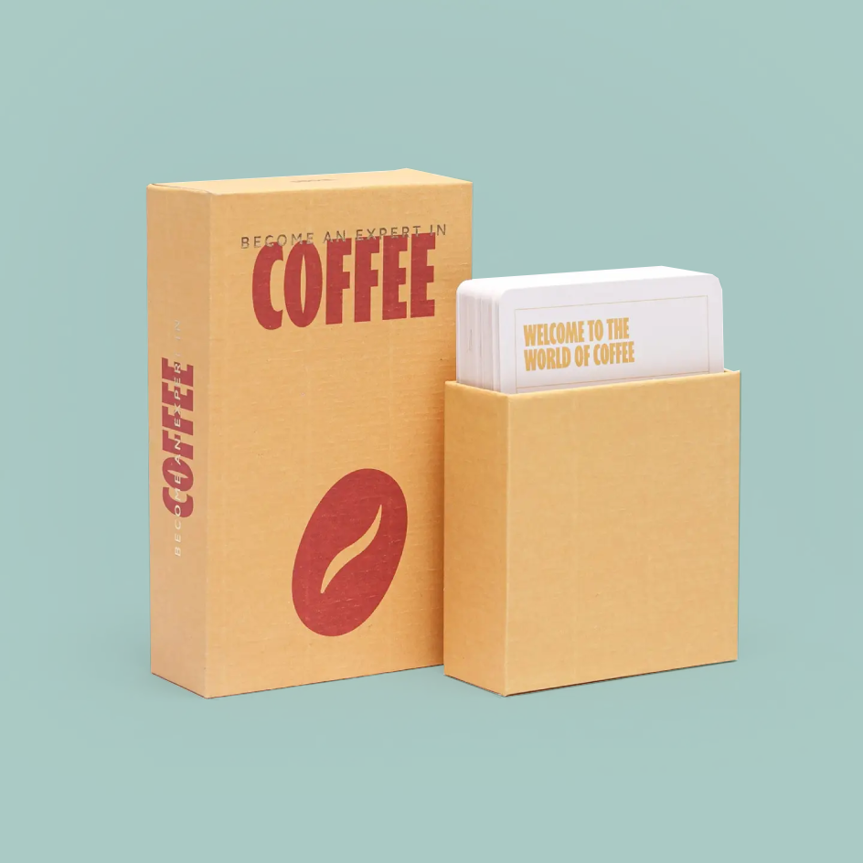 A coffee-themed card deck and its packaging on a solid light teal background. The set includes a tan cardboard box with 'COFFEE' in red, a red coffee bean graphic, and white cards inside a matching tan holder.
