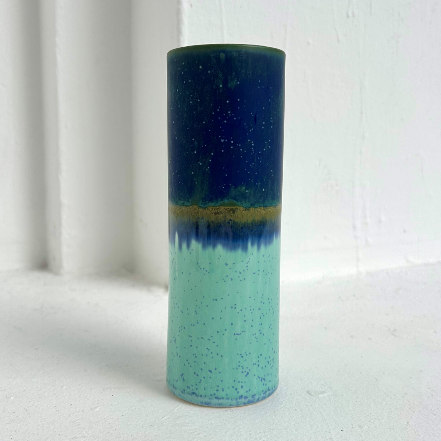 Cylindrical ceramic vase with two-tone blue and green gradient on a white background