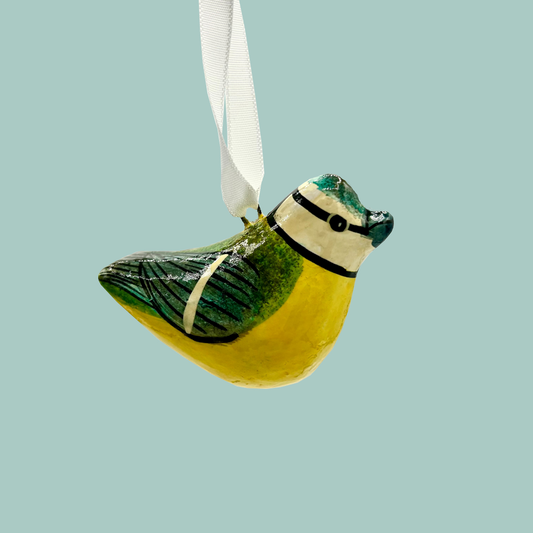 Decorative painted bird with a yellow chest and green wings. Hanging from a white ribbon on a blue background. 
