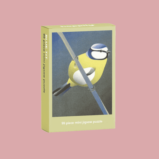 A 99-piece mini jigsaw puzzle box featuring a stylized yellow bird against a muted blue-gray background, shown on a solid dusty pink backdrop.
