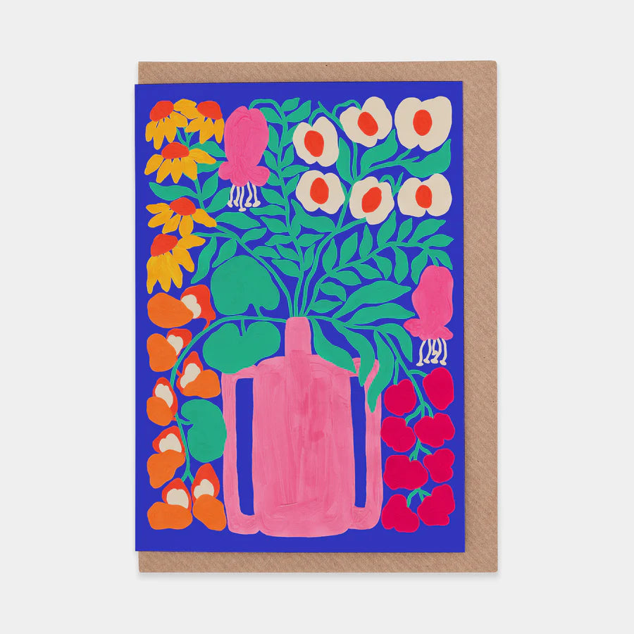A portrait orientation greetings card with an illustration of a pink vase with flowers on a blue background. The card is on a brown envelope on a plain backdrop. 