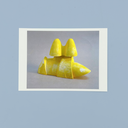 Postcard of a yellow sculpture on a gray background. The postcard is on a blue background.