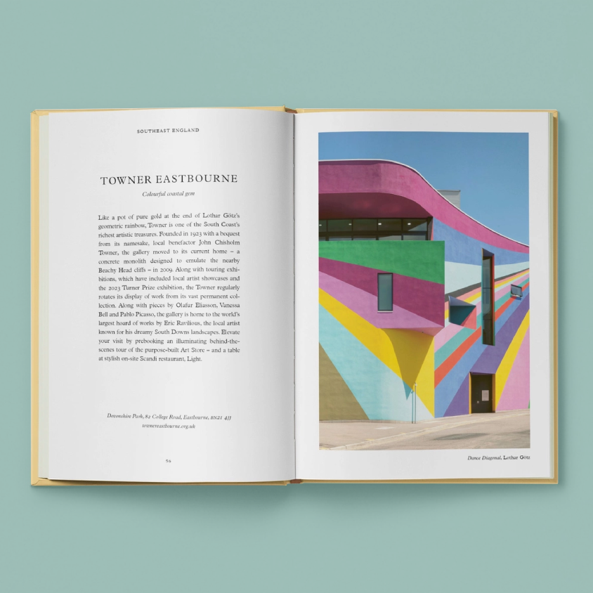 An open book laid flat against a solid pastel teal background. The left page contains black text under the title 'TOWNER EASTBOURNE', and the right page shows a colourful architectural illustration with pink, yellow, blue, and gray geometric forms under a blue sky.