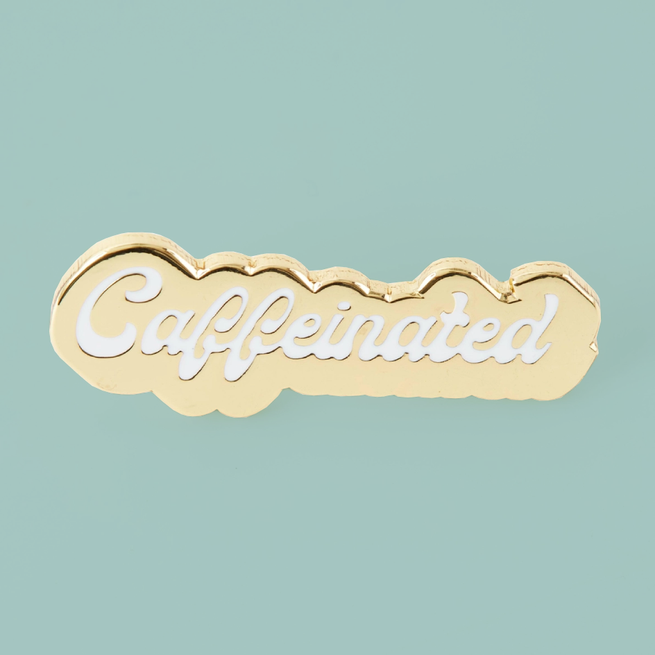 A gold cloud-shaped enamel pin with the word 'Caffeinated' in white script, displayed on a solid light teal background.