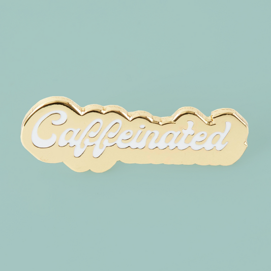 A gold cloud-shaped enamel pin with the word 'Caffeinated' in white script, displayed on a solid light teal background.