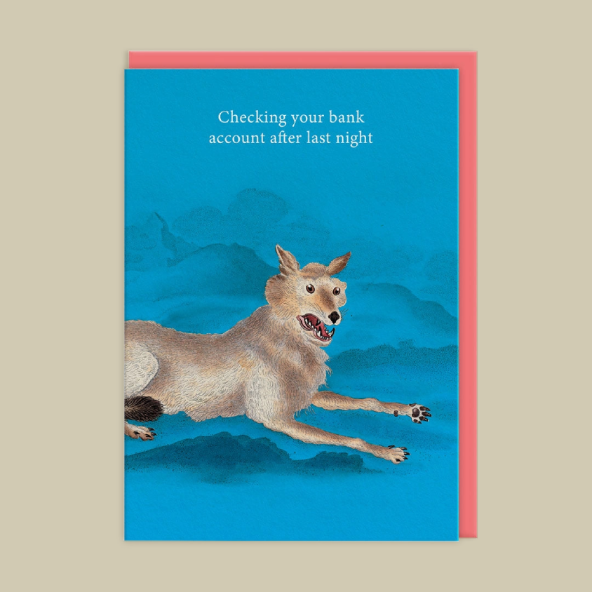 A greeting card featuring a blue illustration of a coyote running across mountains with the text 'Checking your bank account after last night', shown with a pink envelope behind it on a beige background.