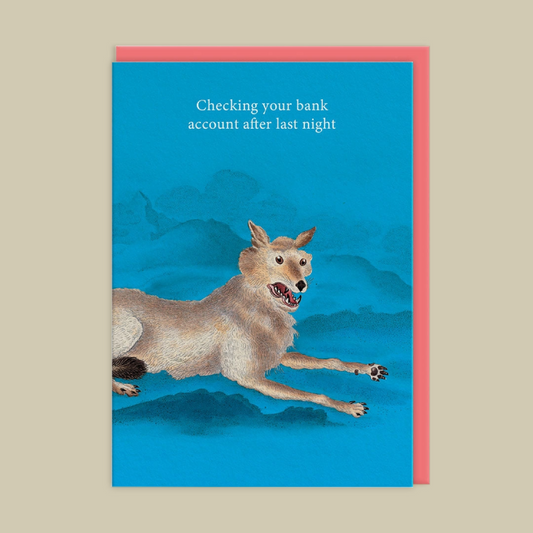 A greeting card featuring a blue illustration of a coyote running across mountains with the text 'Checking your bank account after last night', shown with a pink envelope behind it on a beige background.