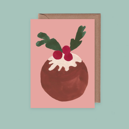 A christmas card with a pink background a painted illustration of a christmas pudding. The card is on a pale teal background.