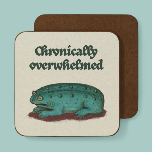 A square coaster with rounded corners featuring the text 'Chronically overwhelmed' above an illustration of a teal amphibian creature, shown in front of a second coaster on a light aqua background.