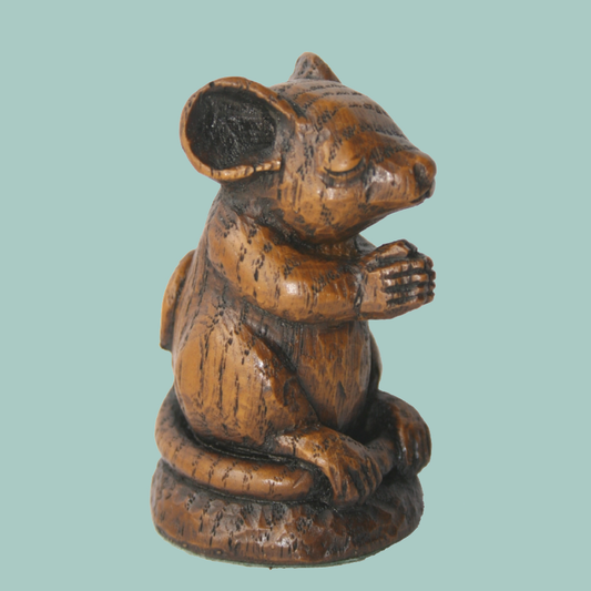 A small carved wooden mouse figurine sitting upright with its paws together, shown against a pale teal background.
