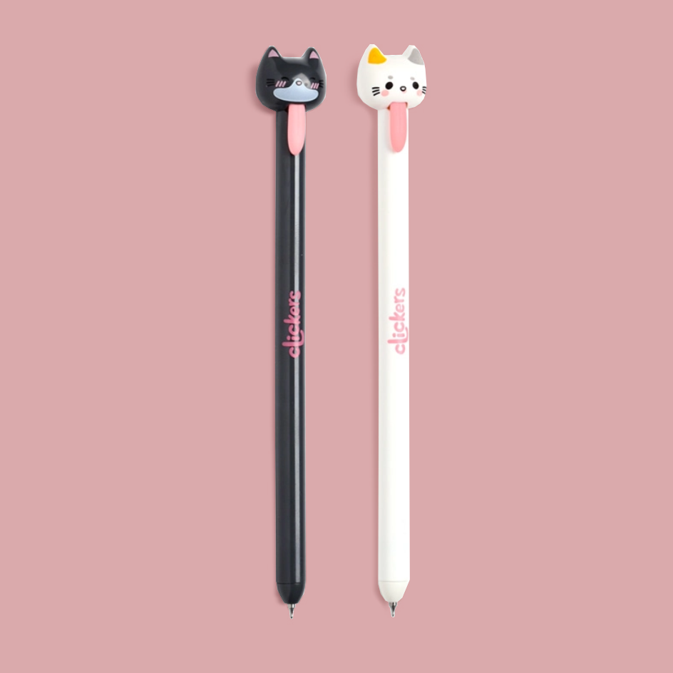 Two novelty pens with 3D cat-shaped tops are shown on a solid dusty pink background. The pen on the left is black with a black cat topper and pink details, and the pen on the right is white with a white cat topper and pink details.