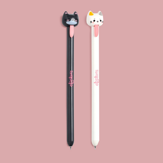 Two novelty pens with 3D cat-shaped tops are shown on a solid dusty pink background. The pen on the left is black with a black cat topper and pink details, and the pen on the right is white with a white cat topper and pink details.